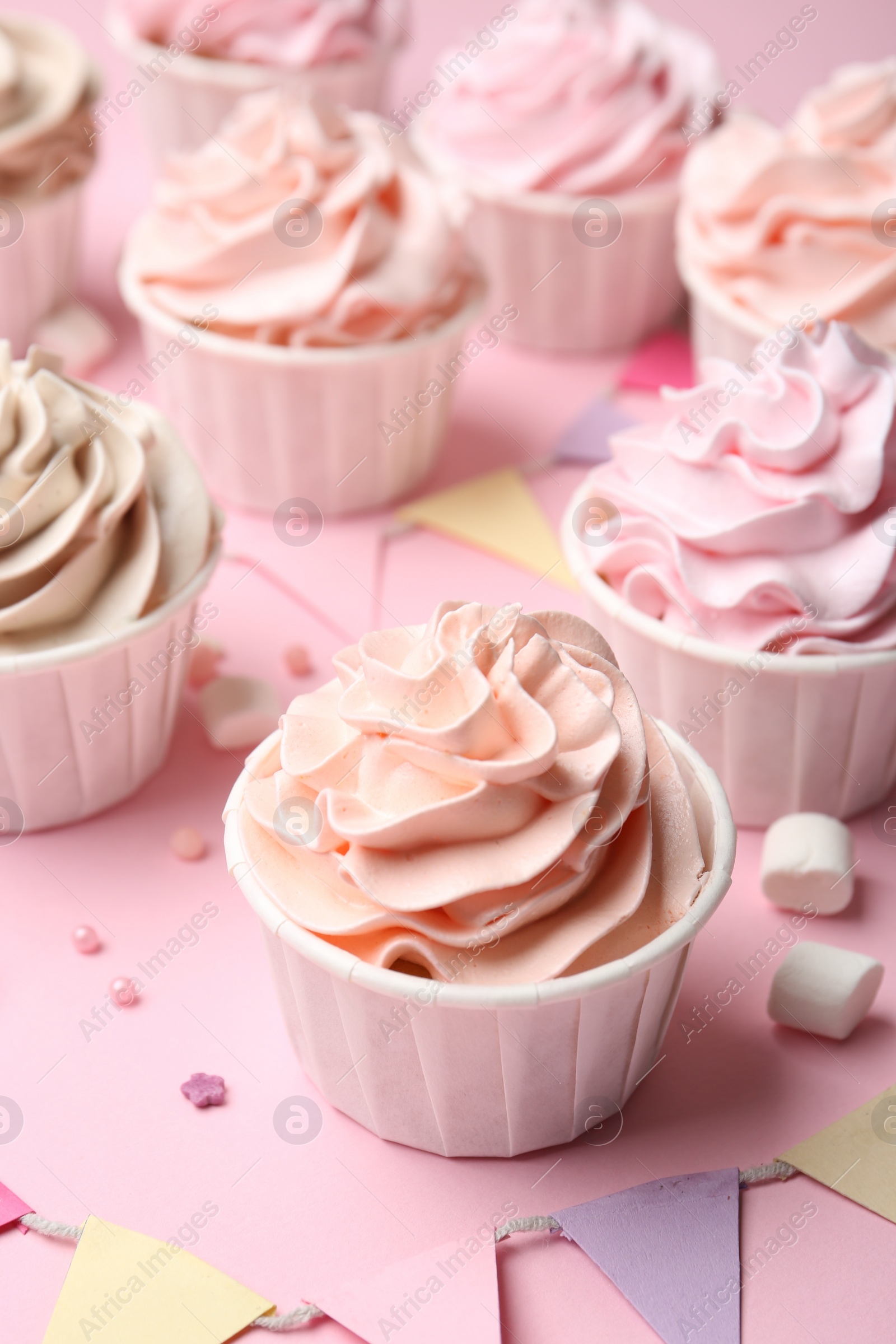 Photo of Delicious birthday cupcakes, bunting flags, marshmallows and sprinkles on pink background, closeup