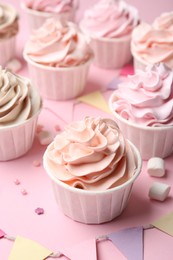 Photo of Delicious birthday cupcakes, bunting flags, marshmallows and sprinkles on pink background, closeup