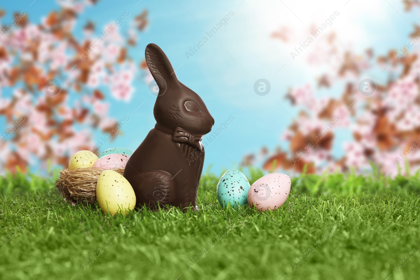 Image of Chocolate bunny and eggs on green grass outdoors. Easter celebration