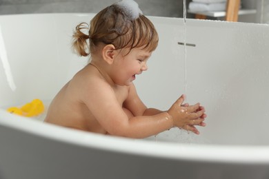Photo of Cute little girl taking bubble bath indoors