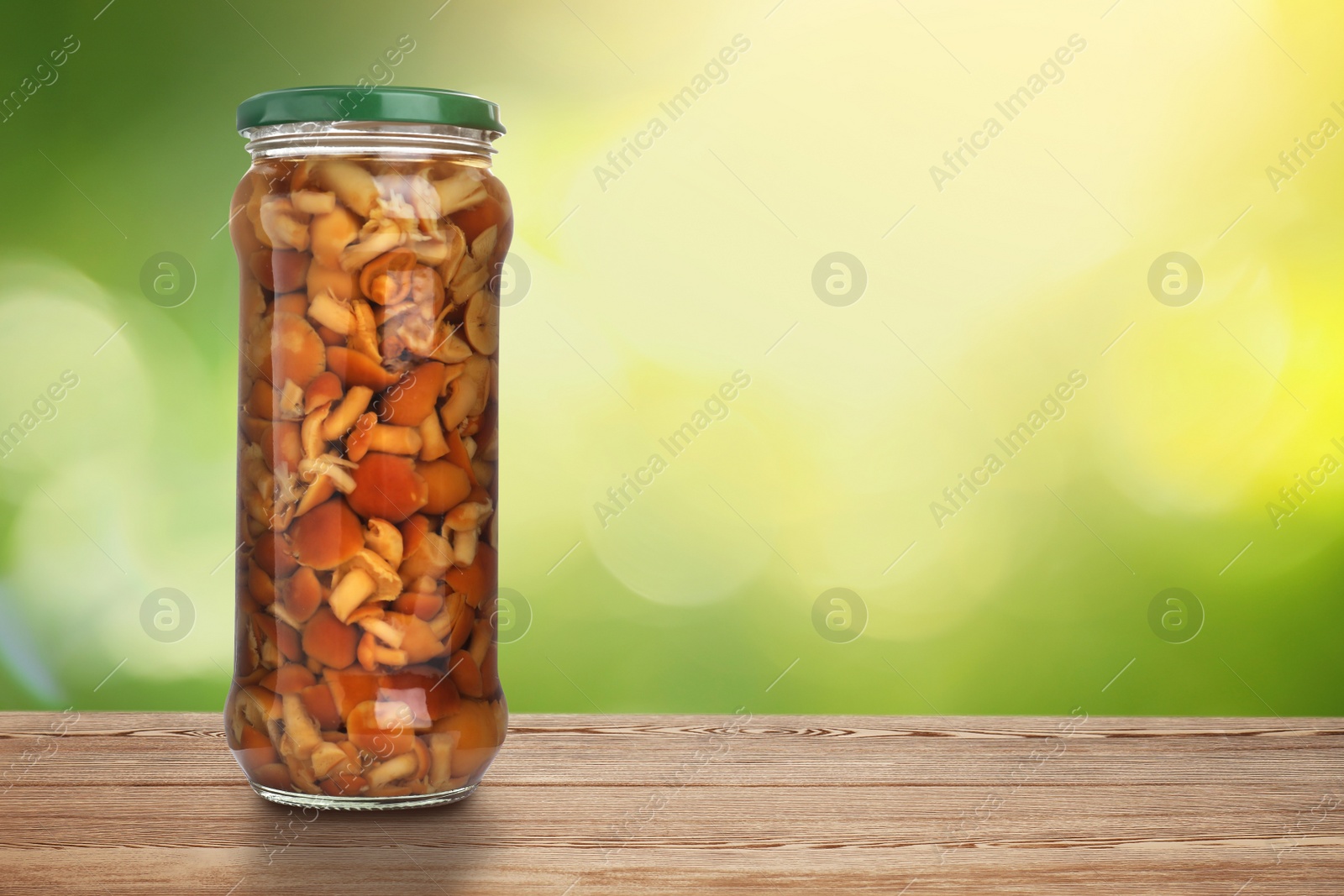 Image of Jar of pickled mushrooms on wooden table against blurred background, space for text