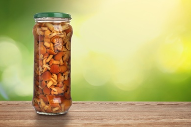 Image of Jar of pickled mushrooms on wooden table against blurred background, space for text