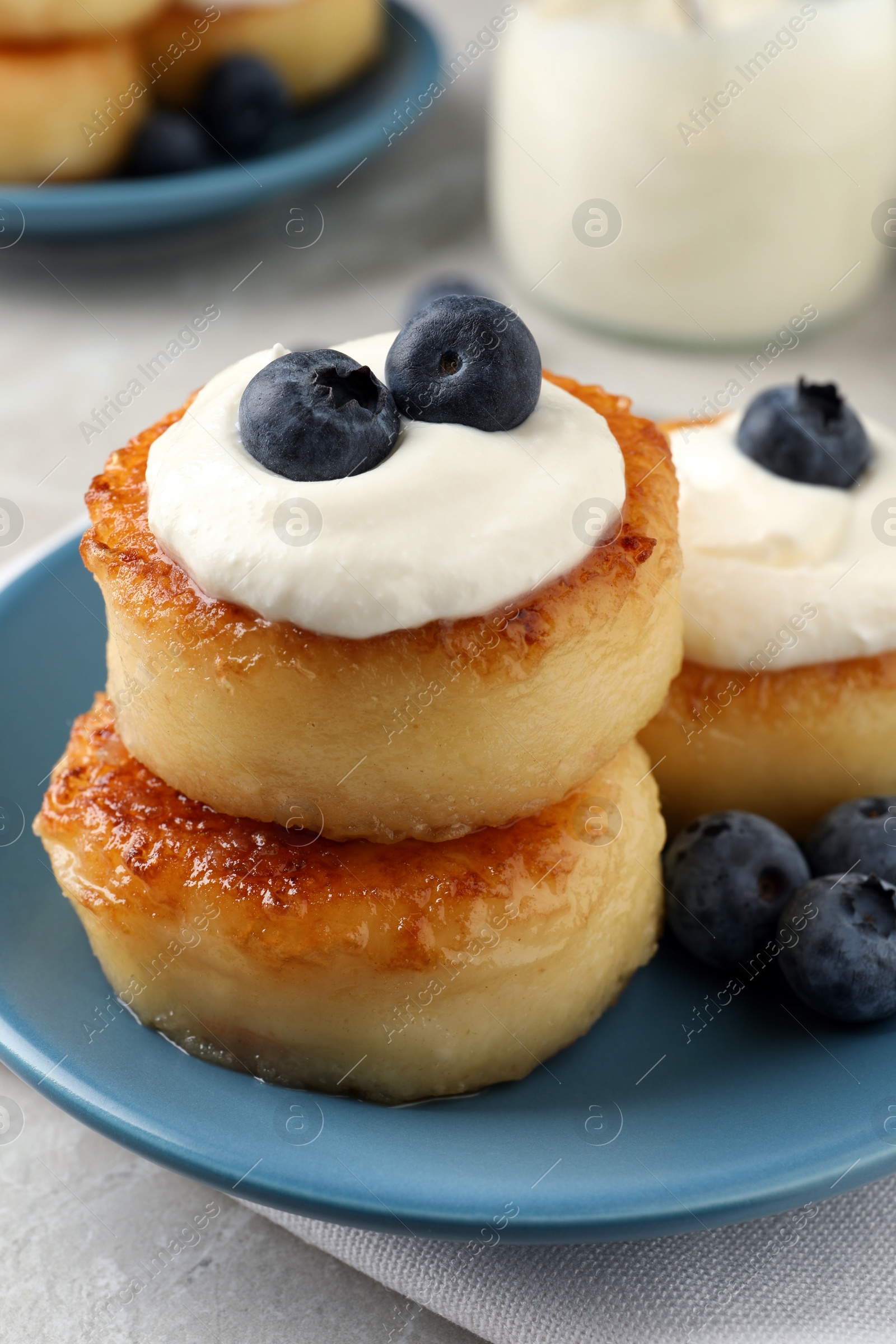 Photo of Delicious cottage cheese pancakes with blueberries, honey and sour cream on light table, closeup