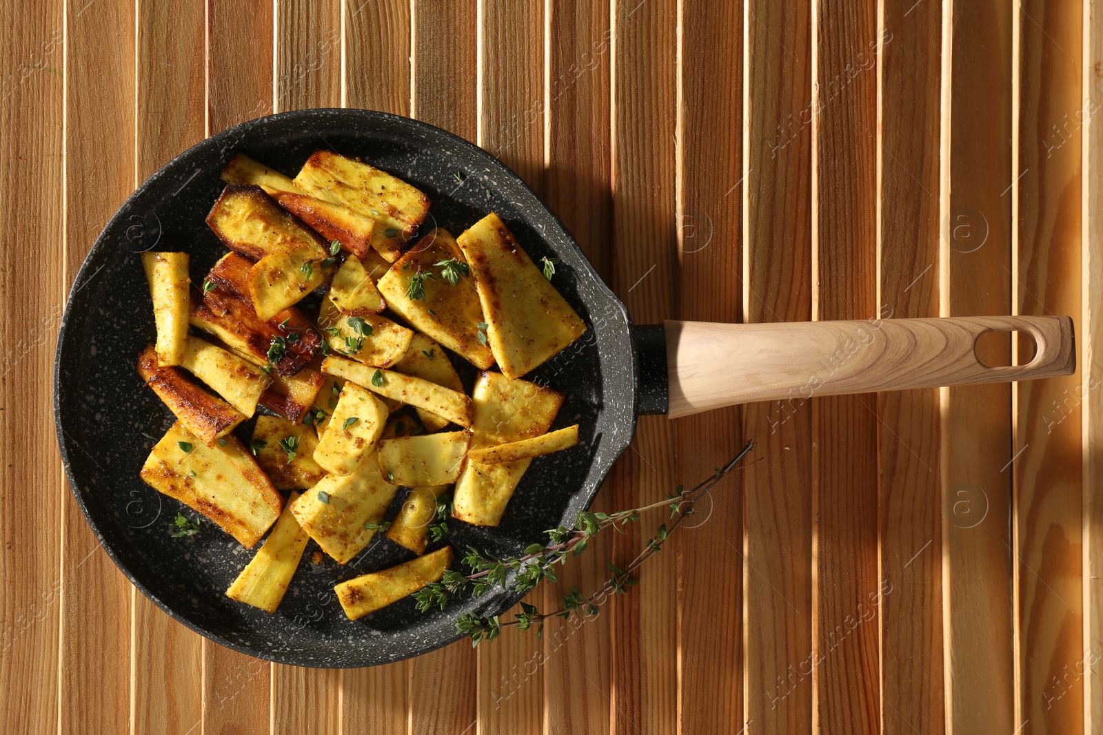 Photo of Delicious parsnips with thyme in frying pan on wooden table, top view