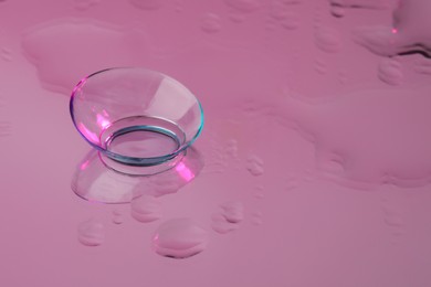 Photo of Contact lens on wet pink reflective surface. Space for text