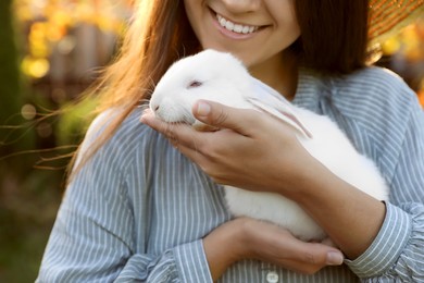 Happy woman holding cute rabbit outdoors on sunny day, closeup