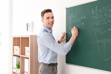 Photo of Young male teacher writing on blackboard in classroom