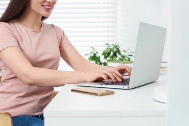 Home workplace. Woman typing on laptop at white desk indoors, closeup