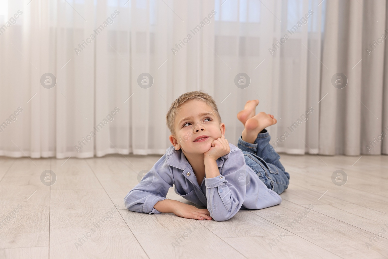 Photo of Cute little boy lying on warm floor at home, space for text. Heating system