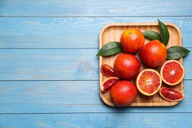 Whole and cut red oranges on light blue wooden table. Space for text