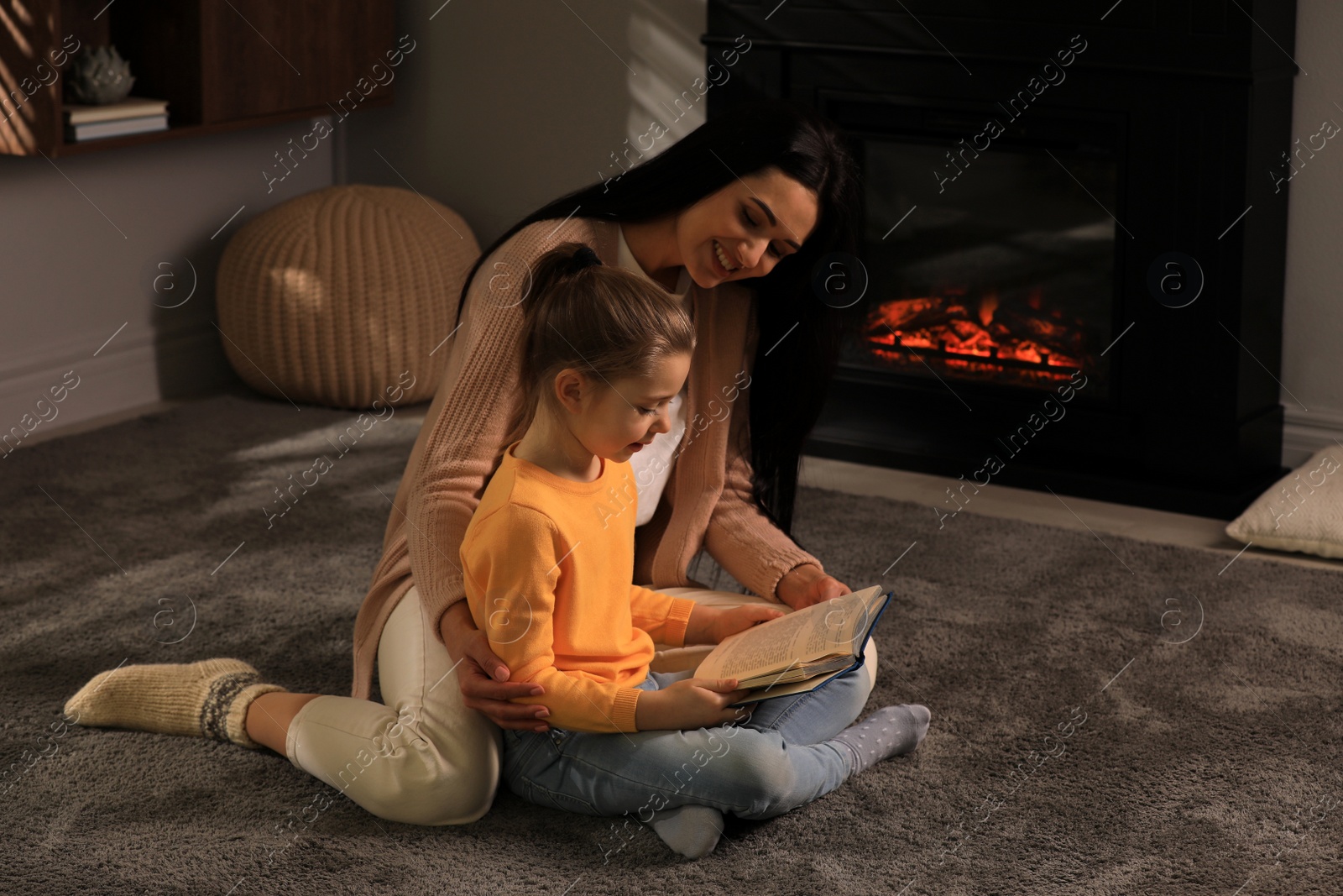 Photo of Happy mother and daughter reading together on floor near fireplace at home