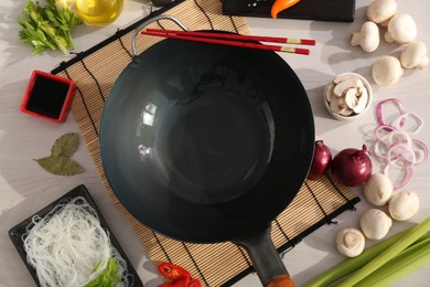 Photo of Wok, chopsticks and different products on white wooden table, flat lay