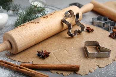 Homemade Christmas biscuits. Raw dough, rolling pin and cookie cutters on grey table, closeup