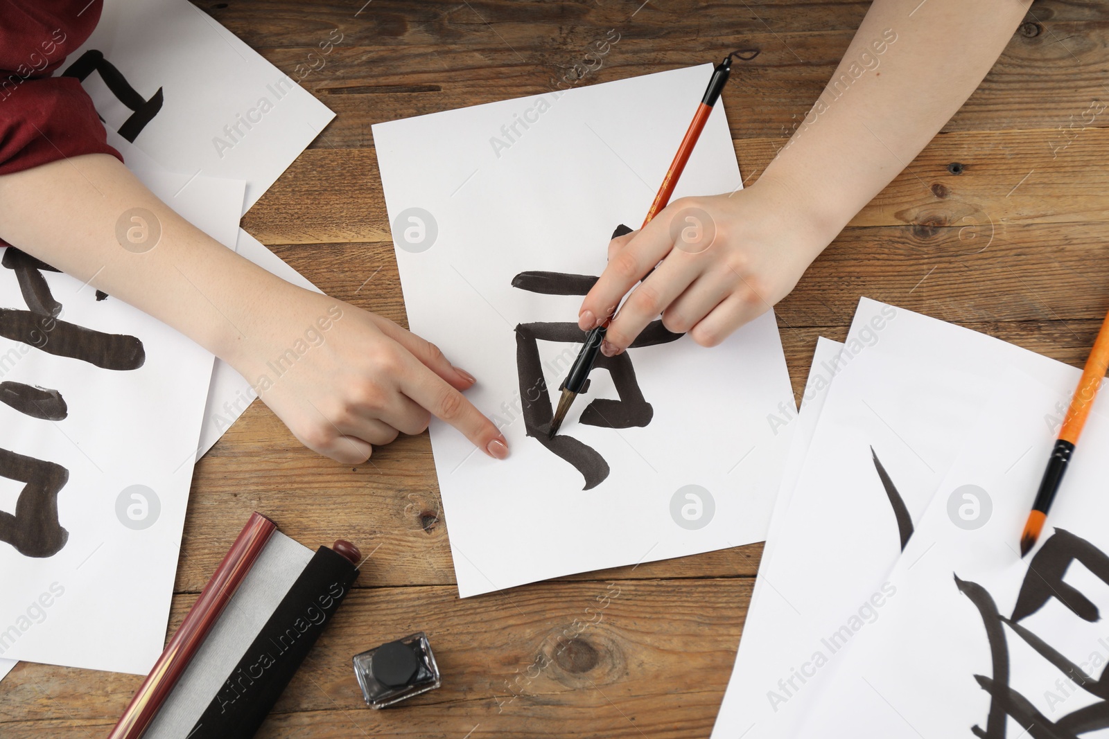 Photo of Calligraphy. Woman with brush and inkwell writing hieroglyphs on paper at wooden table, top view