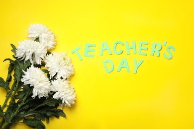 White chrysanthemum flowers and words TEACHER'S DAY on yellow background, flat lay