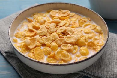 Photo of Bowl of tasty corn flakes on light blue wooden table, closeup