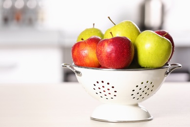 Photo of Colander with different sweet apples on table in kitchen, closeup. Space for text