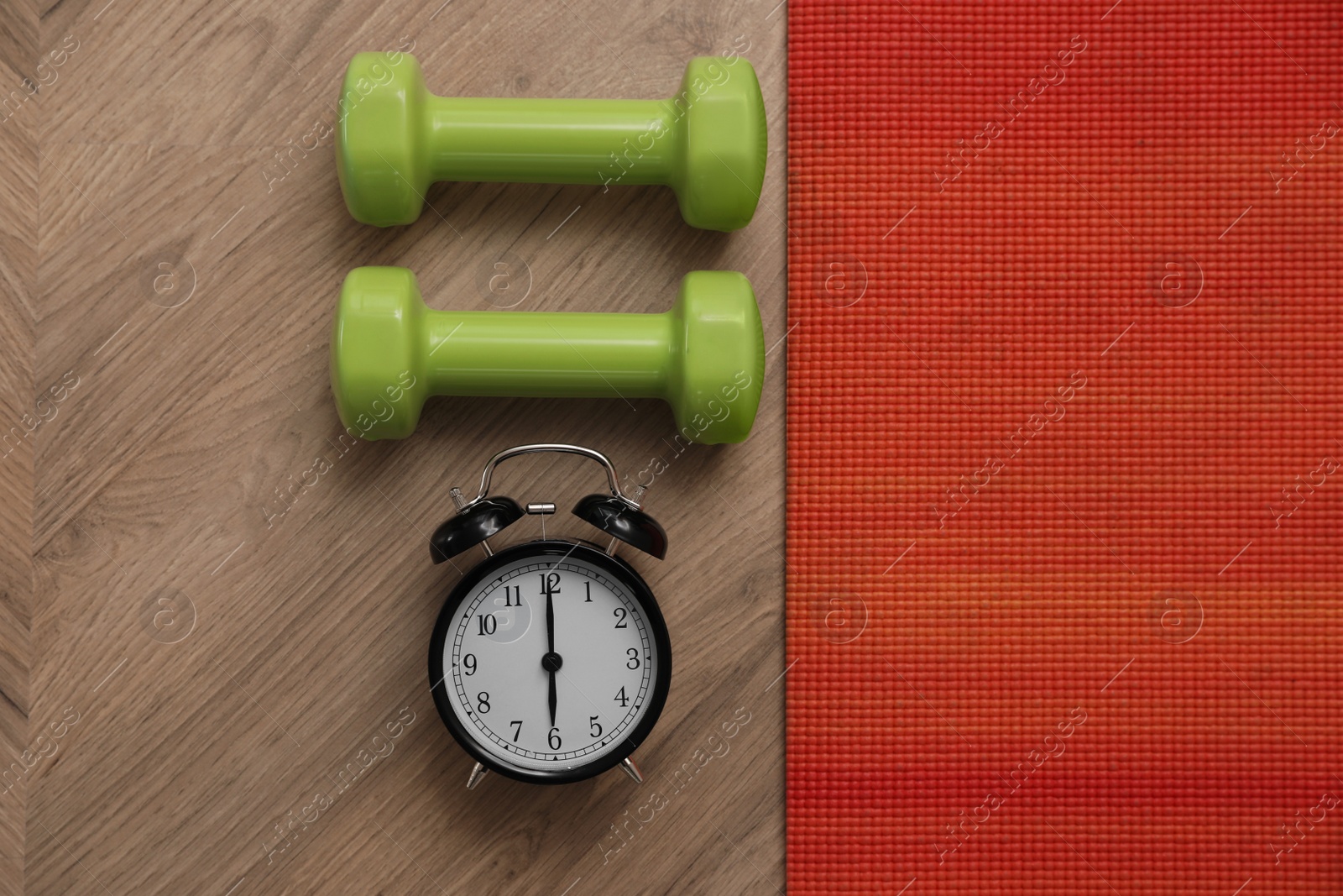 Photo of Alarm clock, yoga mat and dumbbells on wooden background, flat lay. Morning exercise