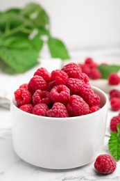 Bowl with fresh ripe raspberries on white marble table, closeup
