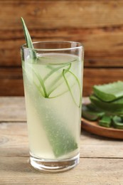 Photo of Tasty aloe juice and cut fresh leaves in glass on wooden table, closeup