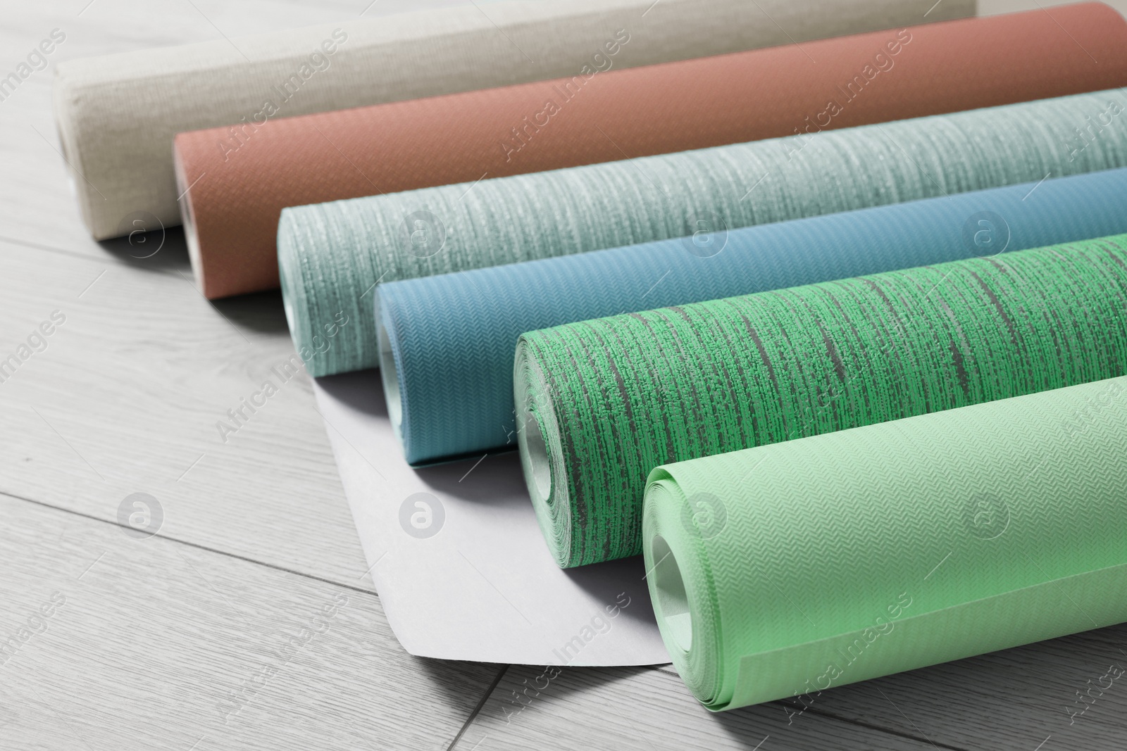 Image of Colorful wallpaper rolls on light wooden floor, closeup
