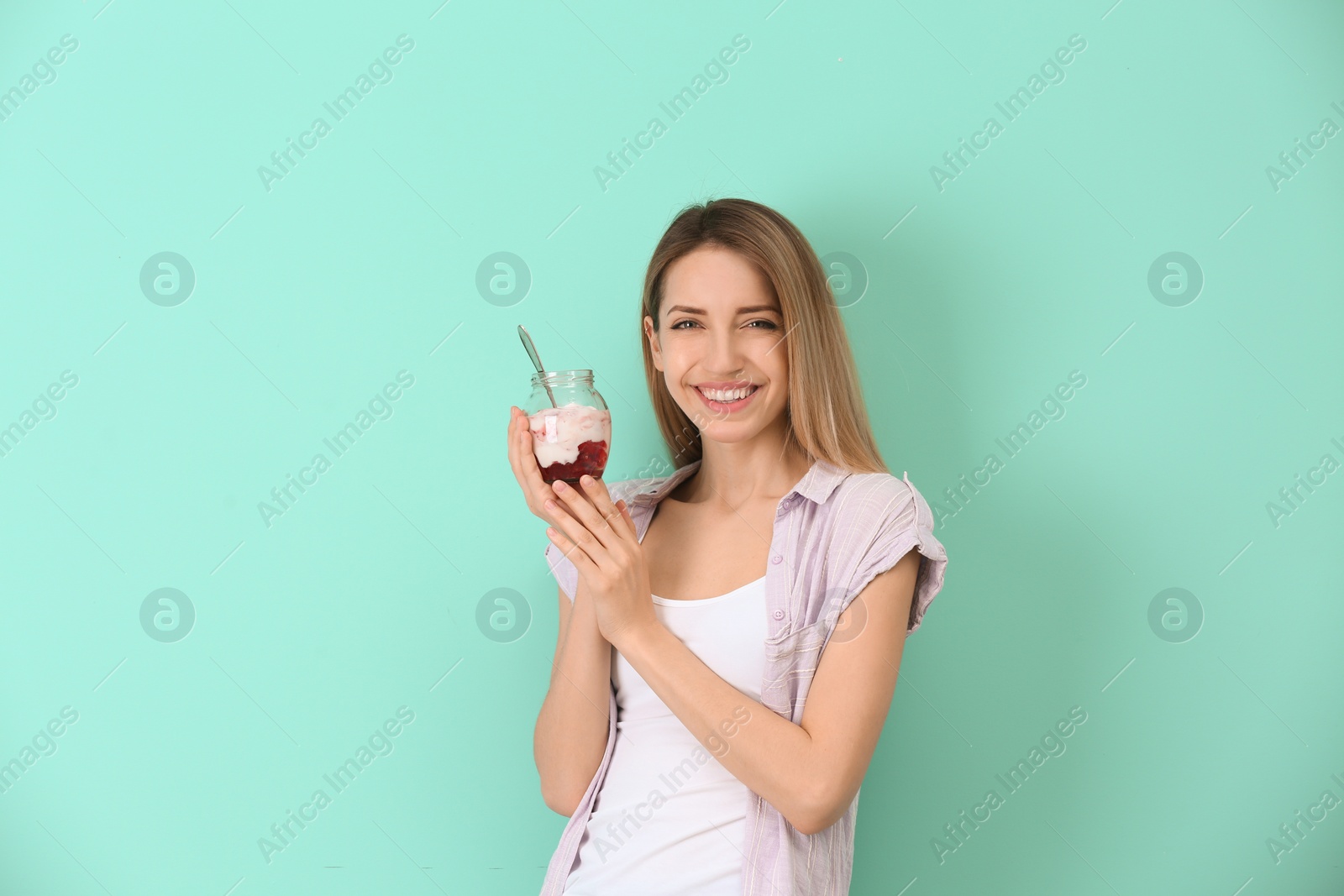 Photo of Young attractive woman eating tasty yogurt on color background