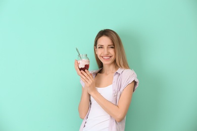 Young attractive woman eating tasty yogurt on color background