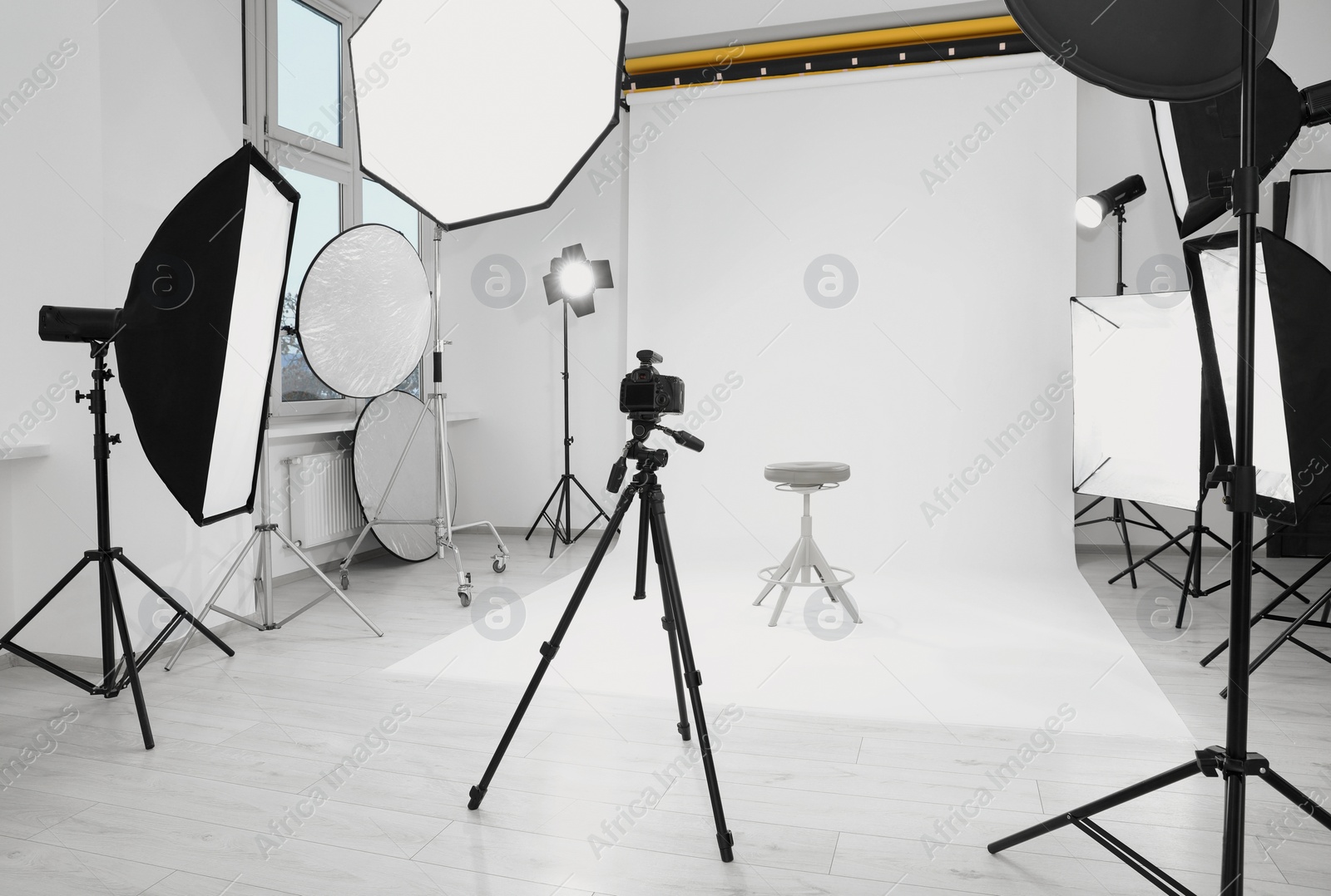 Photo of Tripod with camera, bar stool and professional lighting equipment in modern photo studio