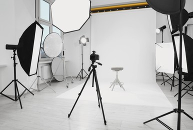 Tripod with camera, bar stool and professional lighting equipment in modern photo studio