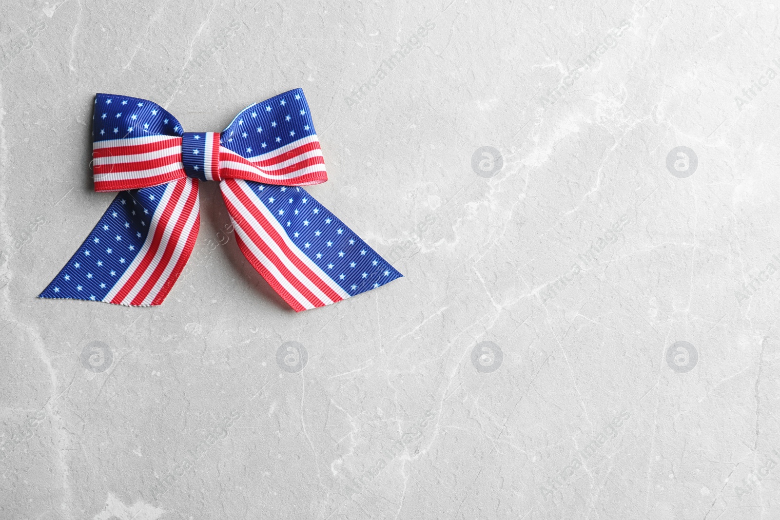 Photo of Ribbon bow with American flag pattern on light background, top view with space for text. USA Independence Day