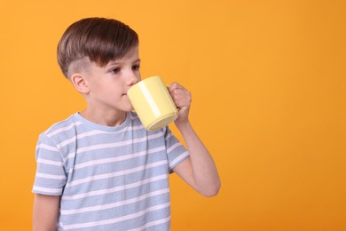 Cute boy drinking beverage from yellow ceramic mug on orange background, space for text