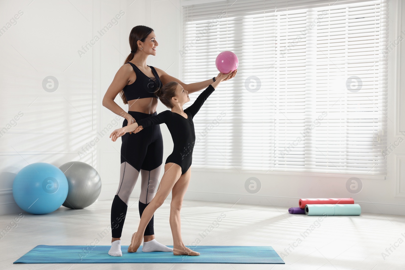 Photo of Gymnastic coach helping little girl to do exercise with ball indoors
