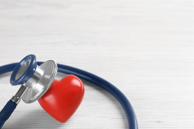 Photo of Stethoscope and red heart on white wooden table, closeup with space for text. Cardiology concept