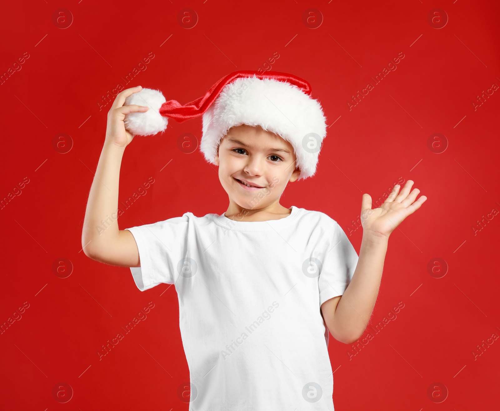 Photo of Cute little child wearing Santa hat on red background. Christmas holiday