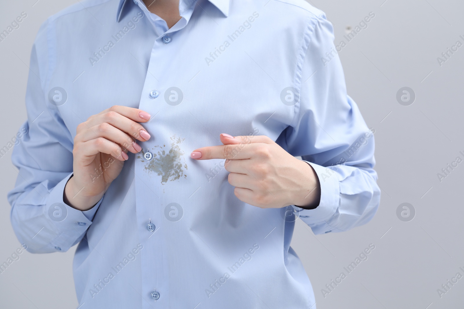 Photo of Woman showing stain on her shirt against light grey background, closeup