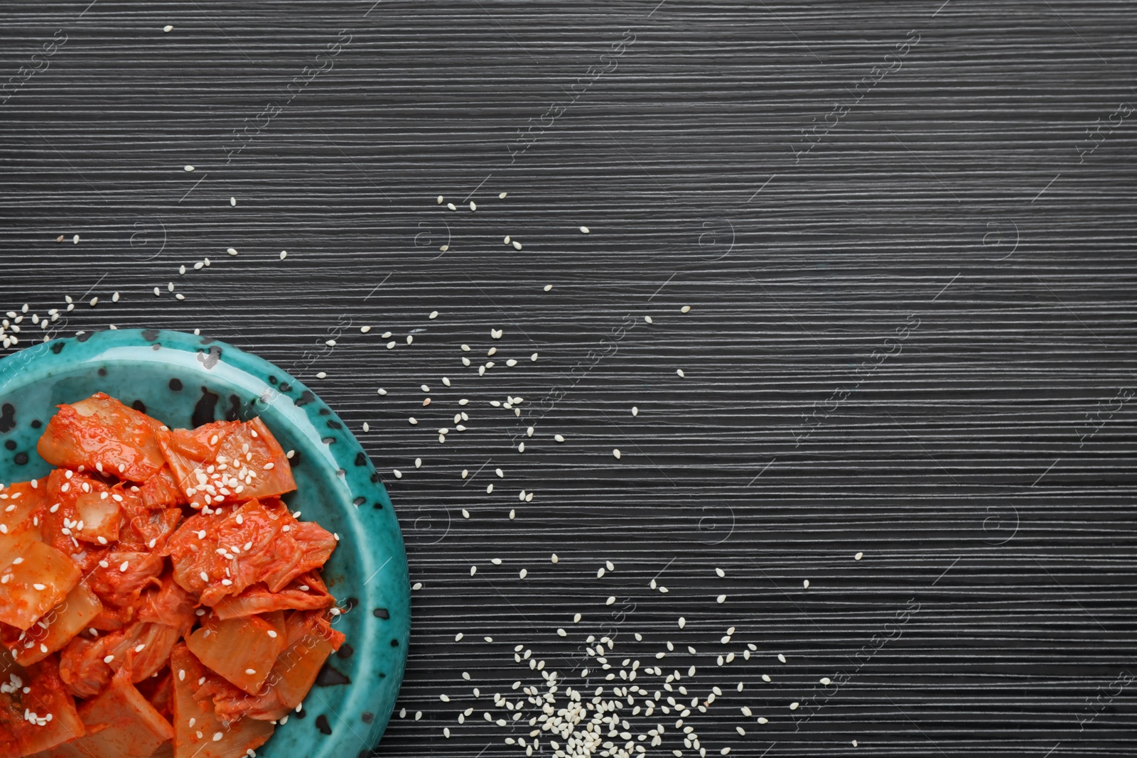 Photo of Plate of spicy cabbage kimchi and sesame seeds on black wooden table, flat lay. Space for text