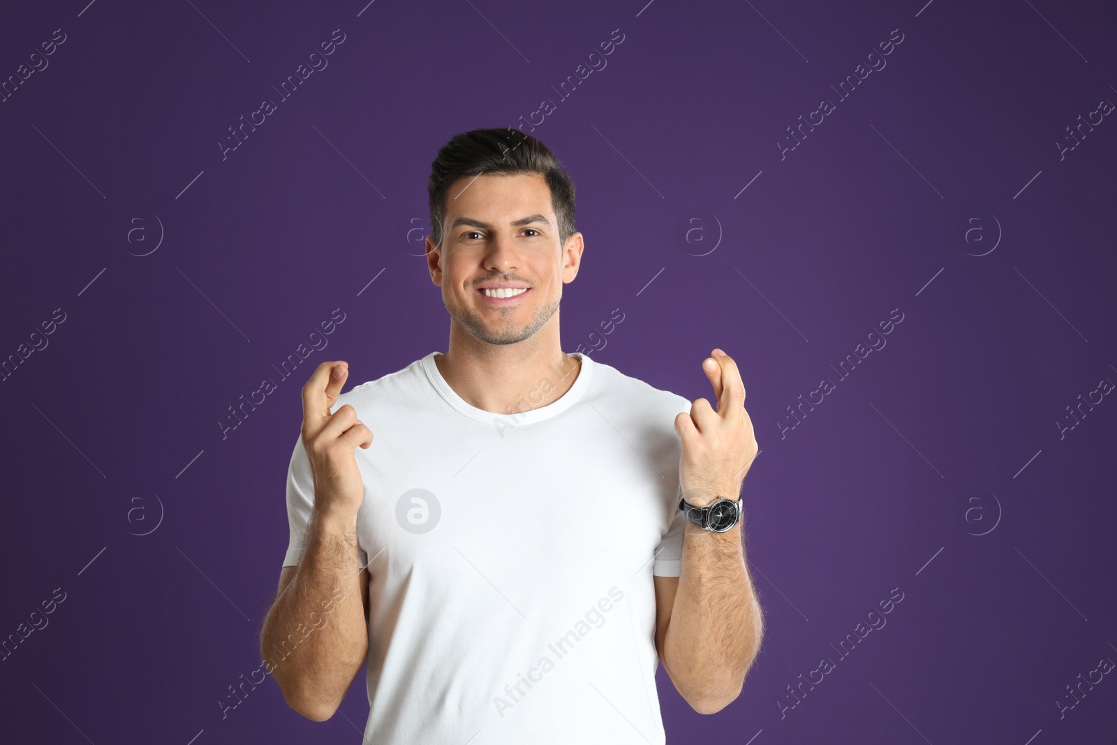 Photo of Man with crossed fingers on purple background. Superstition concept