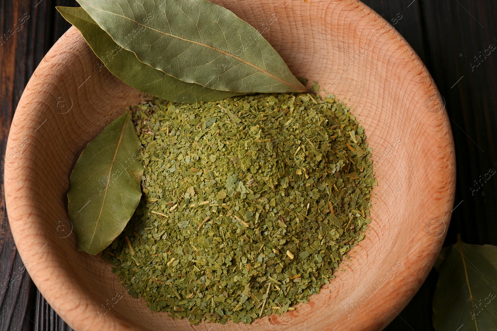 Photo of Whole and ground aromatic bay leaves in wooden bowl, top view