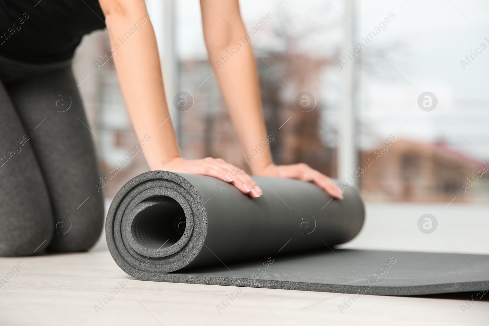 Photo of Woman rolling yoga mat on floor indoors, closeup