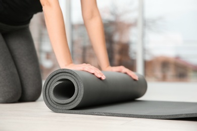 Photo of Woman rolling yoga mat on floor indoors, closeup