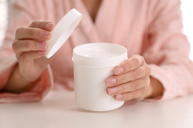 Photo of Woman with jar of moisturizing cream at white table, closeup