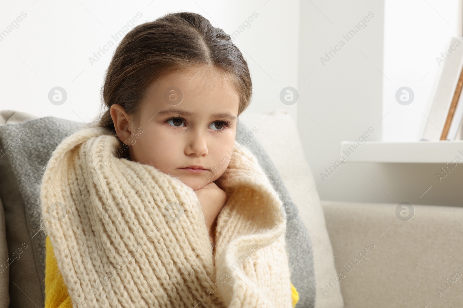 Photo of Girl with scarf around neck on sofa in room. Cold symptoms