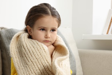 Girl with scarf around neck on sofa in room. Cold symptoms