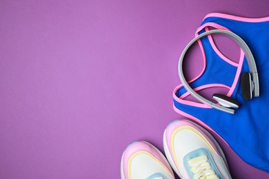 Photo of Stylish sportswear and headphones on purple background, flat lay. Space for text