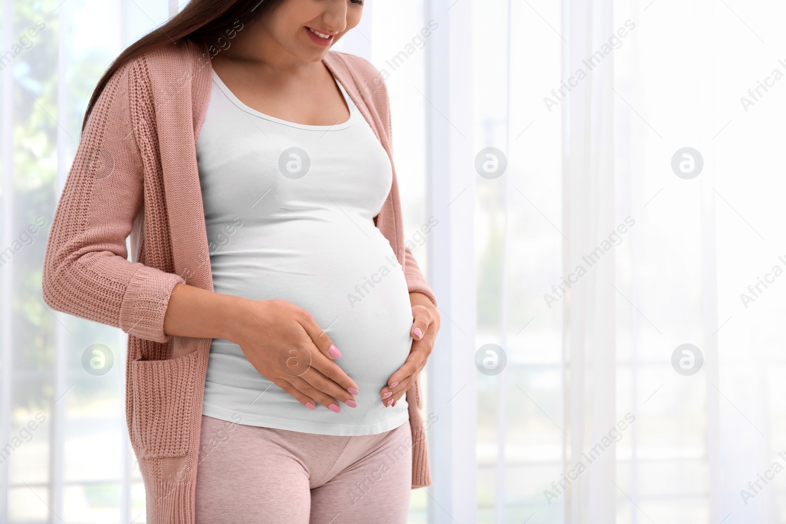 Photo of Young pregnant woman near window at home, closeup