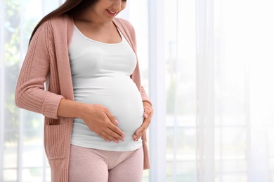 Young pregnant woman near window at home, closeup