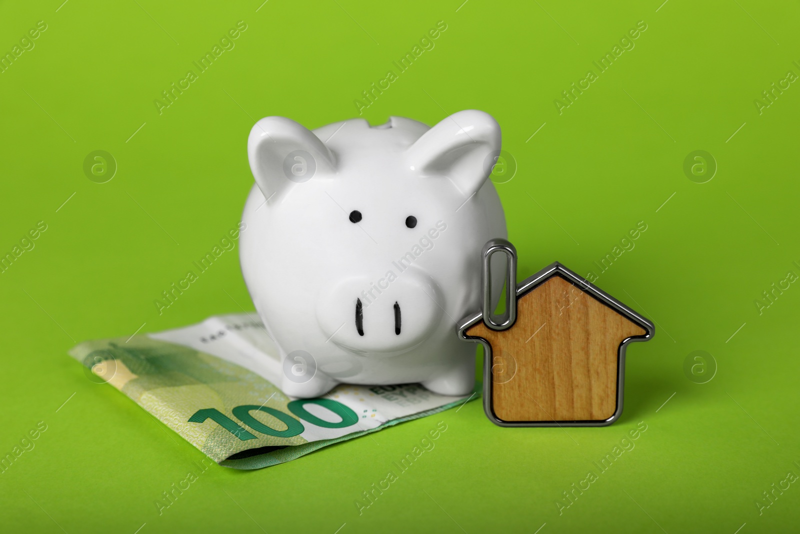 Photo of Ceramic piggy bank, euro banknote and key trinket on light green background. Financial savings