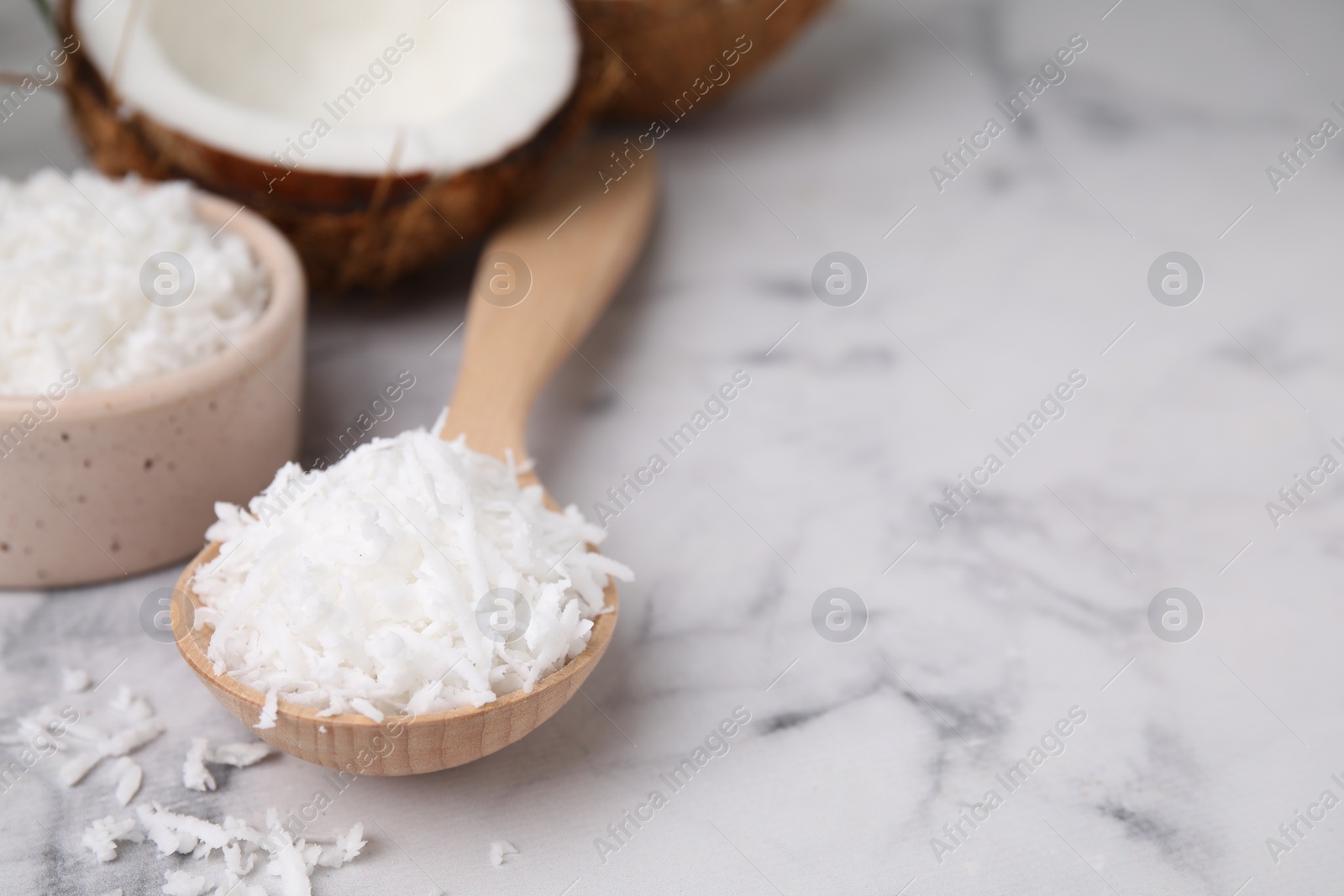Photo of Coconut flakes in wooden spoon on white marble table, closeup. Space for text