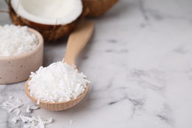 Coconut flakes in wooden spoon on white marble table, closeup. Space for text