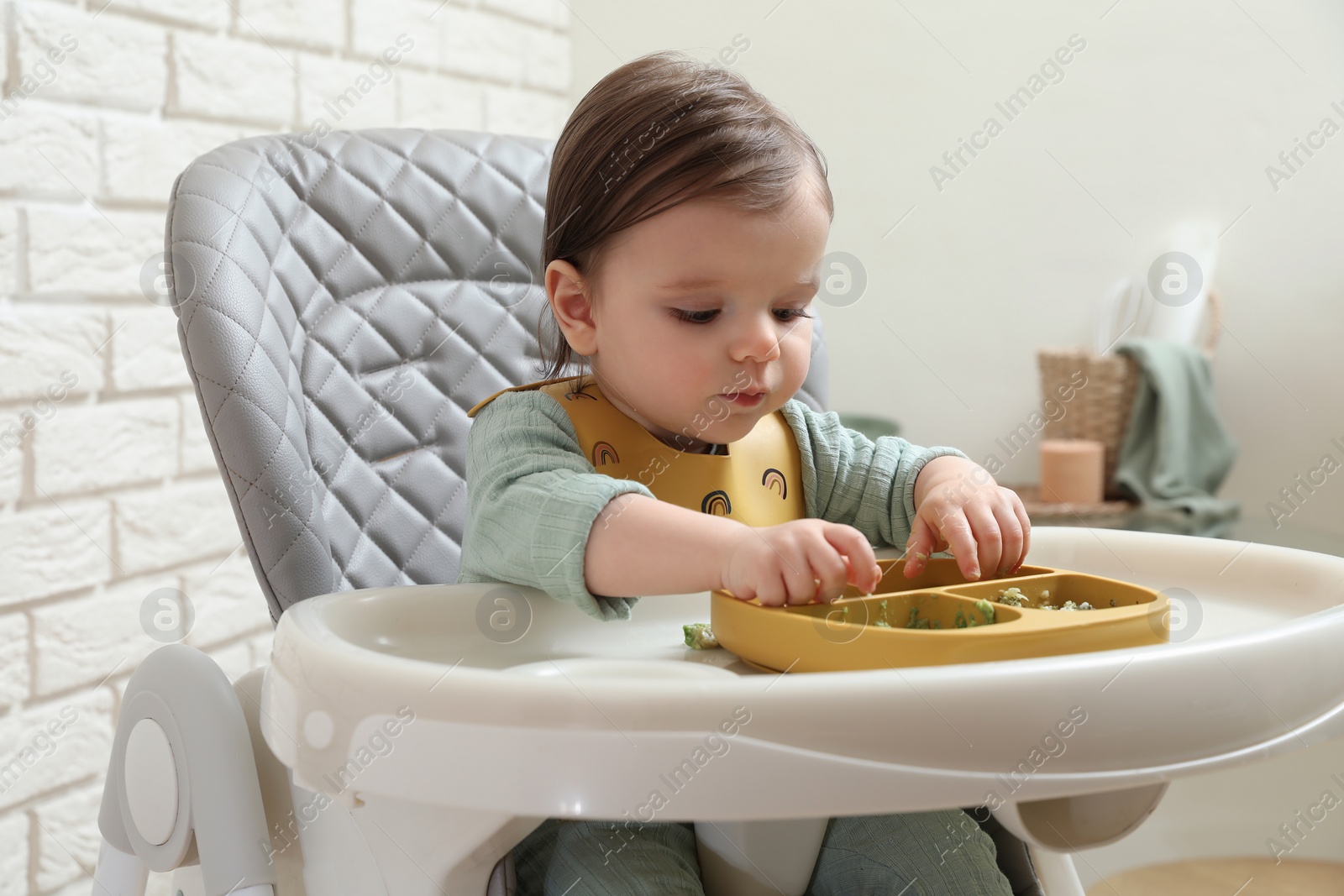 Photo of Cute little baby eating healthy food in high chair indoors